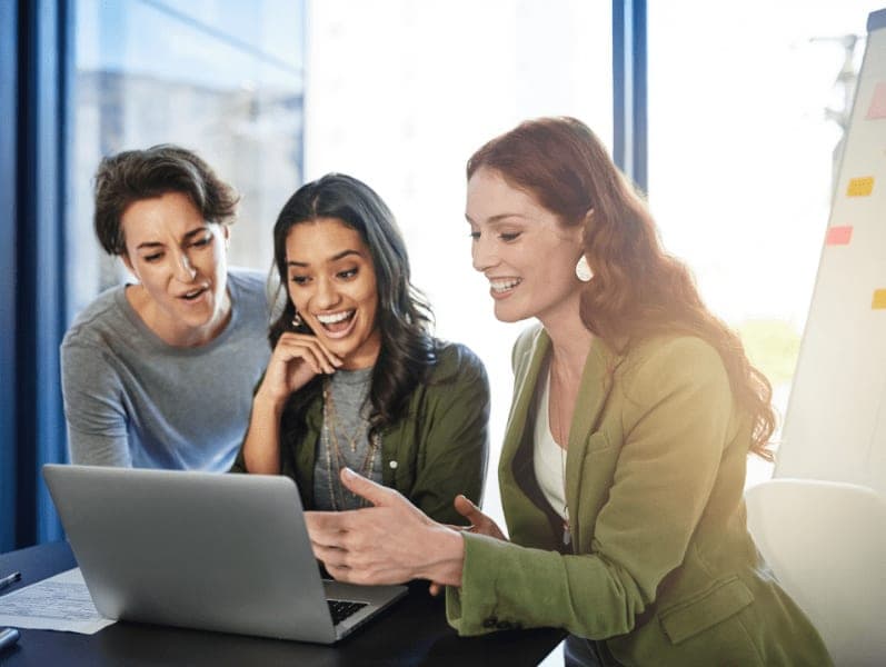 Females sitting around lap top smile at new cloud workflow that they are reviewing
