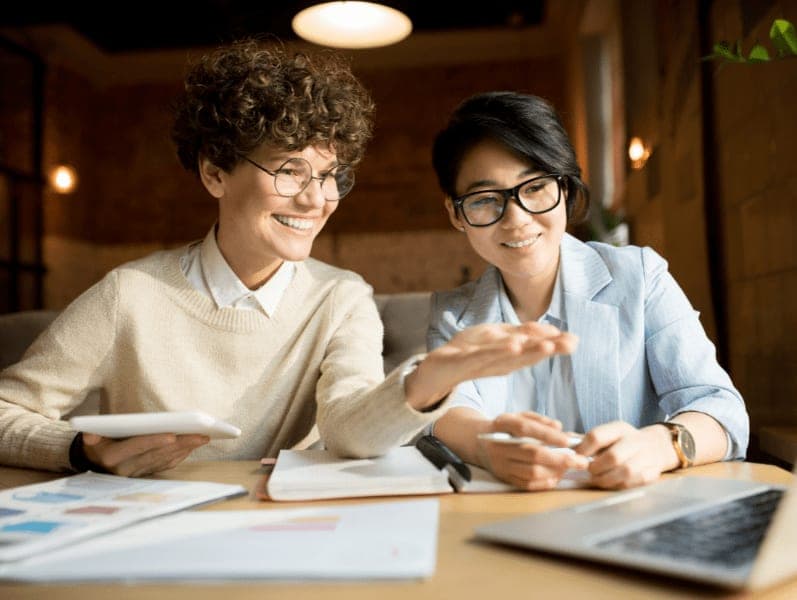 Female colleagues sitting beside each other reviewing items on a laptop