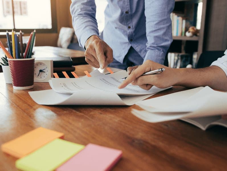 Two people leaning over a desk with papers with only there arms in view