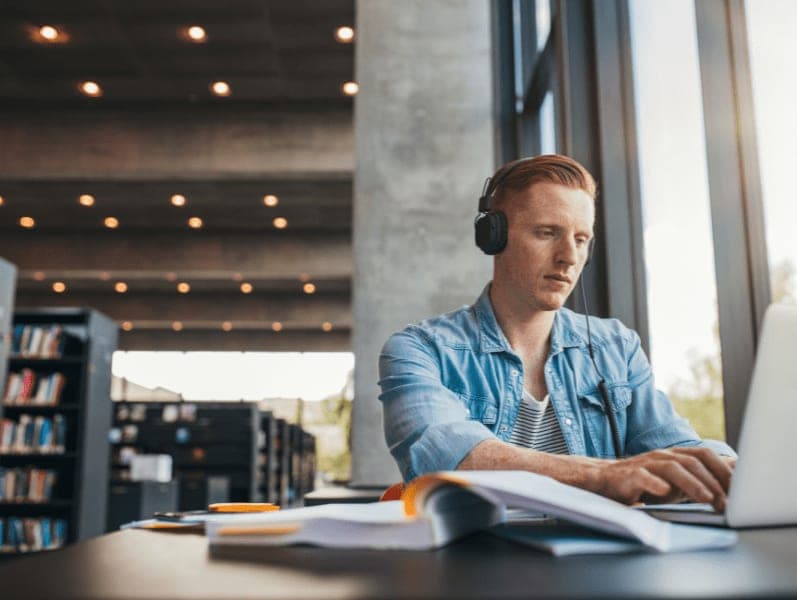 Young male sitting in library study for exam on his laptop