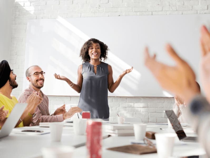 Woman standing at the head of the table speaking with a group of people