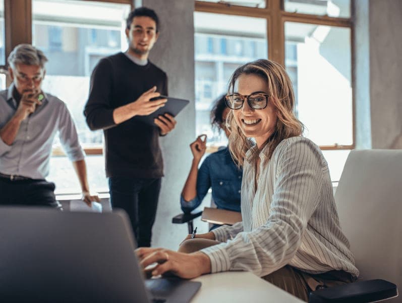 Female sitting at desk with colleagues sitting around referencing a marketing plan