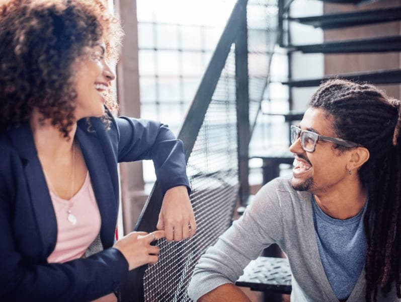 Female facing male colleague sitting on stairs engaging in a happy conversations