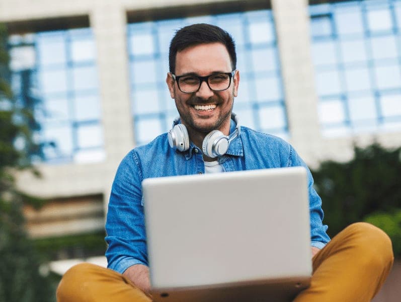 Man sitting outside with legs crossed smiling with laptop on legs