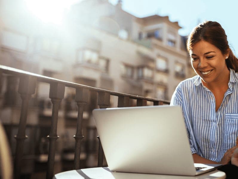 Female remote worker sitting out side on balcony in front of laptop