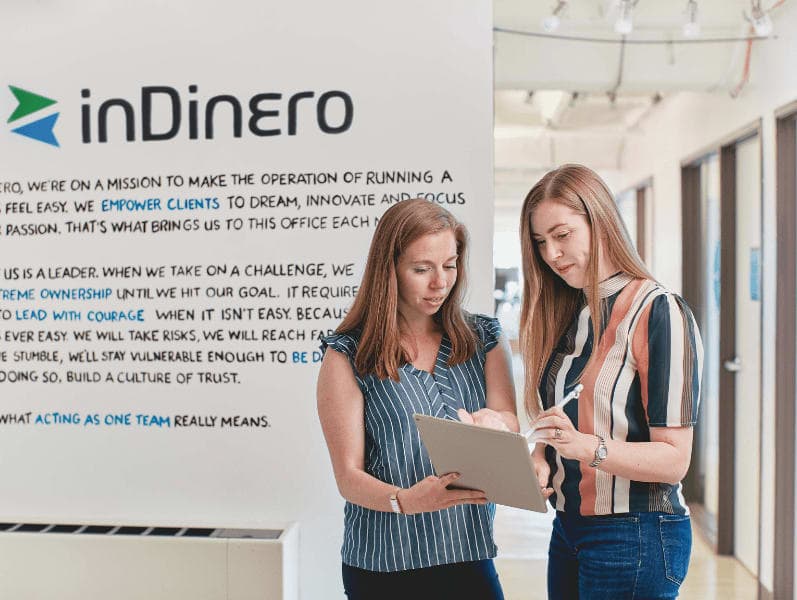 Two colleagues standing in front entrance of office referencing to a tablet in front of them
