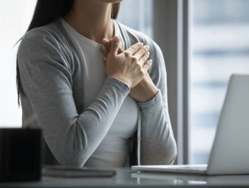 Female torso with hands-on her heart while sitting in front of her laptop