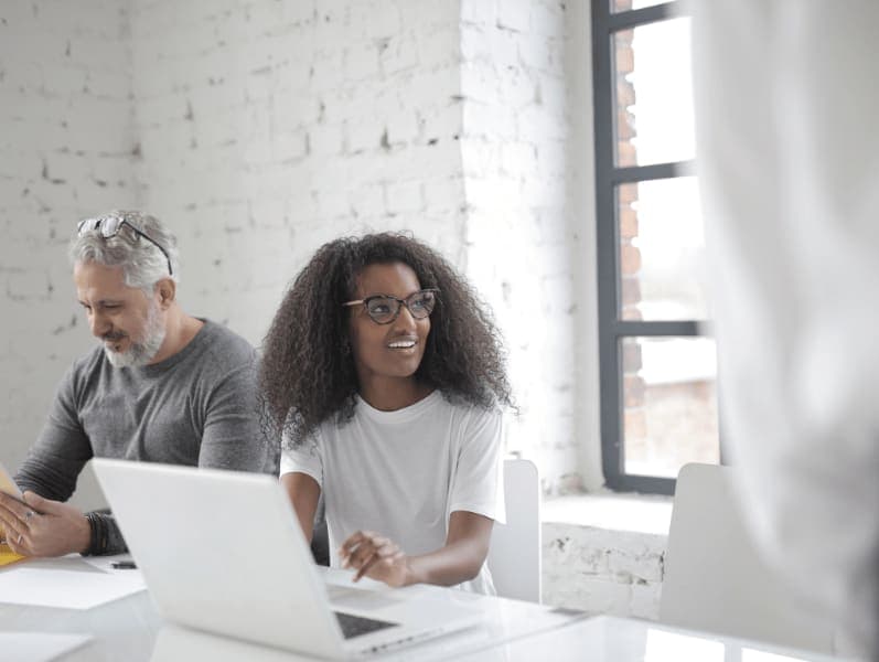 Female looking up at presenter, while working on her laptop as male colleague site beside her