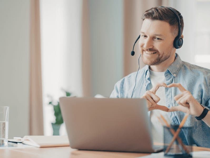 Male colleague calling in via laptop making a heart symbol with hands