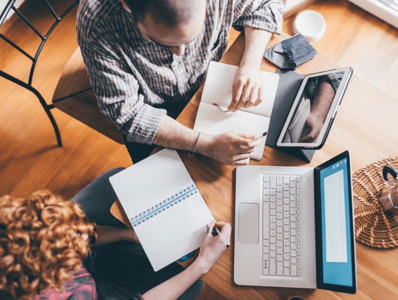 area view of male and female sitting at a table working on a laptop and note book