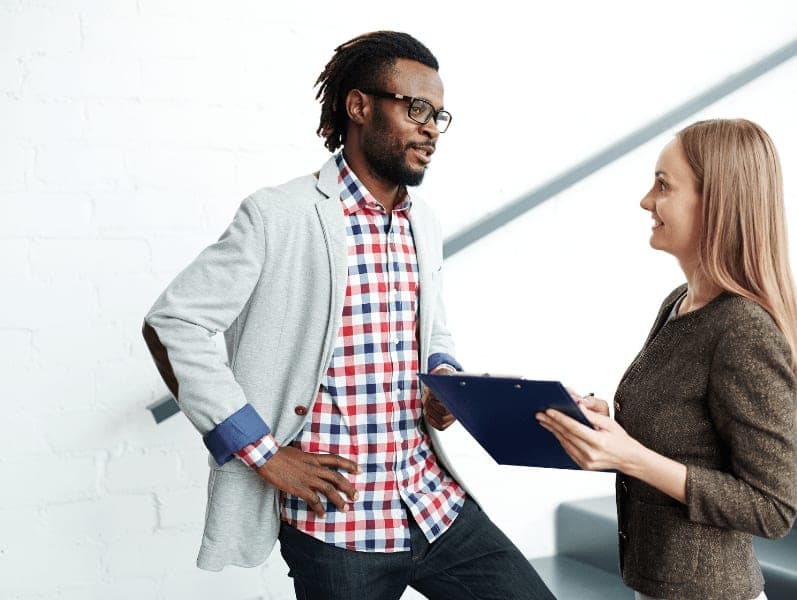 side view of male and female colleague meeting at bottom of stairs to review something