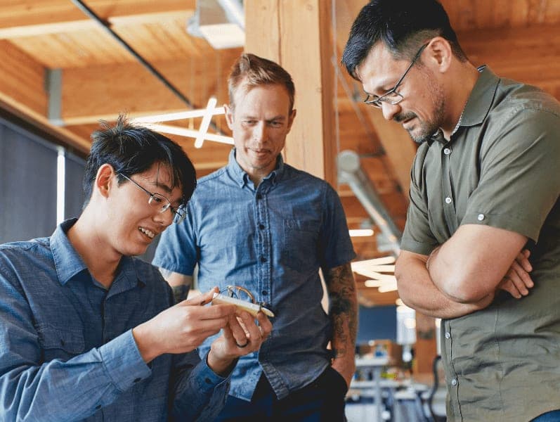 Three male colleagues standing together looking at a device