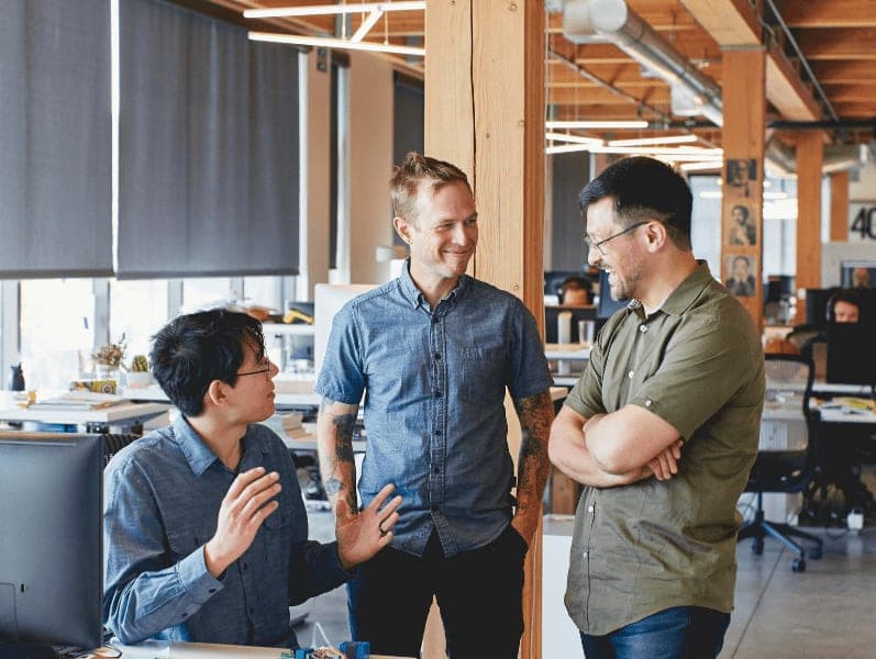 Three male colleagues standing in office facing each other while having a conversations