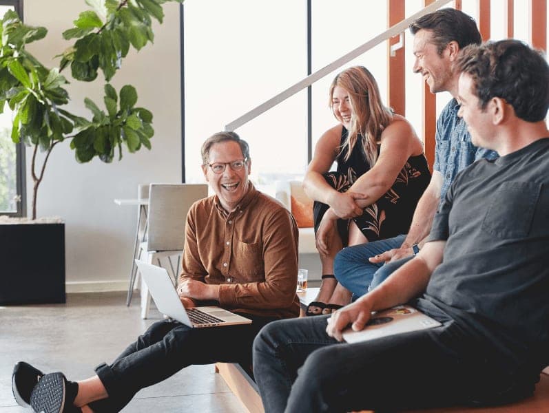 Senior male leader sitting on bottom of stairs surrounds by other collogues smiling