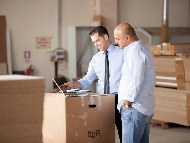Two male leaders in a warehouse referencing her lap during a conversation