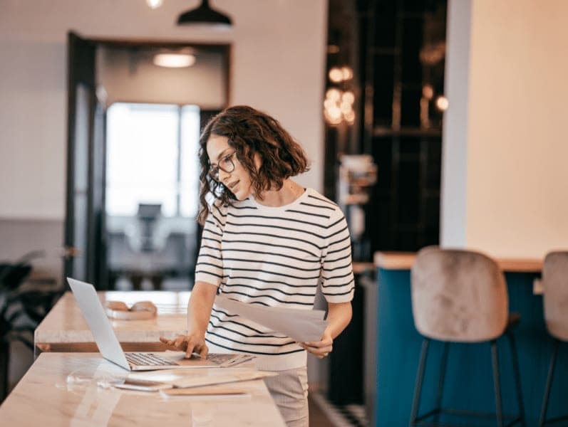 Woman standing at Island table while working on her laptop while talking on her cell phone