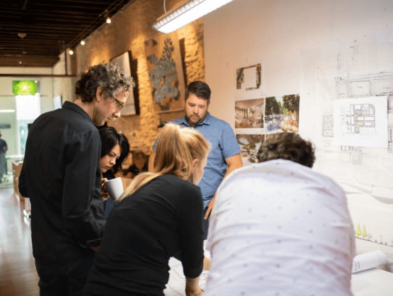 A group of 6 male and female colleagues meeting and standing over a table looking at a project