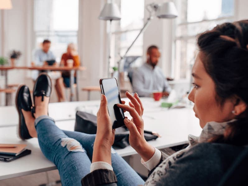 Portrait side view of a female sitting with her feet up on a desk on her phone