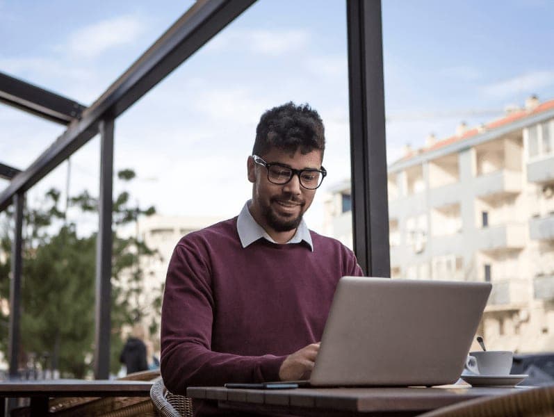 Man with glasses sitting in outdoor cover area with laptop