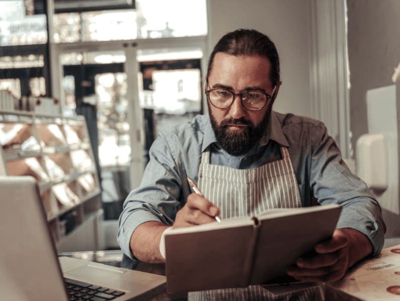 Male bake shop owner sitting at desk reviewing notes in a note book