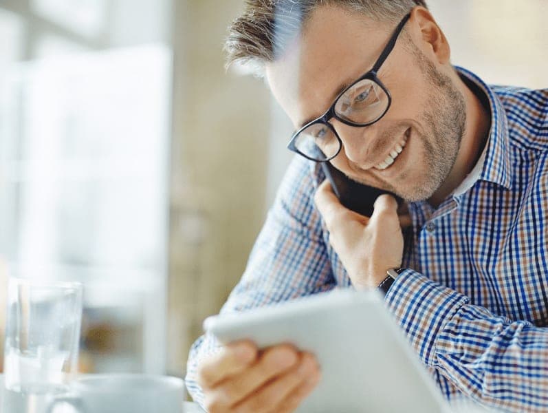 Middle aged man with glasses talking on his cell phone while reference details on his ipad.