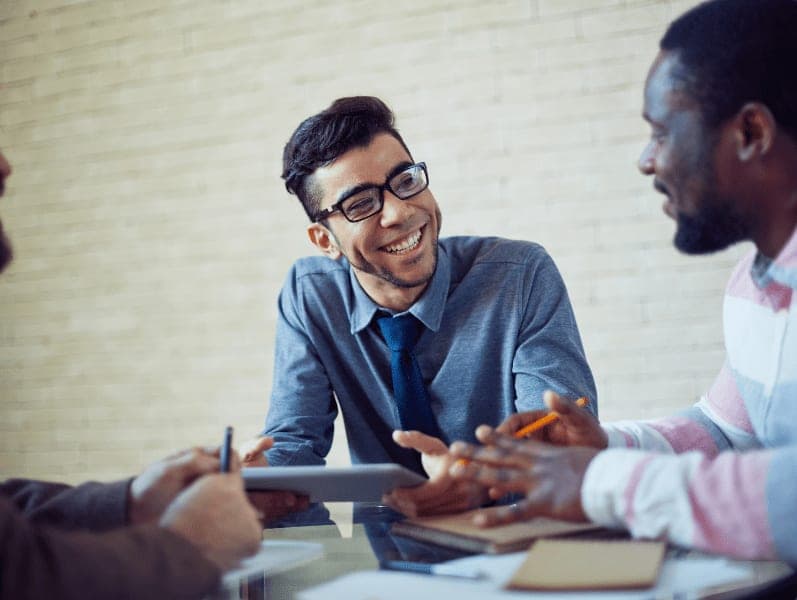 Two men sitting at a table smile as they are discussing a topic over an ipad